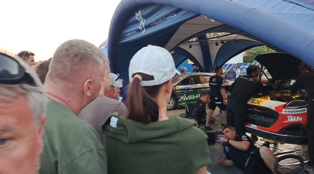Fani vēro Seska ekipāžas auto steidzīgo remontu
